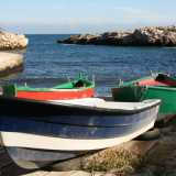 Le tipiche barche dei pescatori, colorate di verde e rosso o bianco e blu, sono ormeggiate su una spiaggia di pietre e ciottoli chiari che si stempera in un meraviglioso mare blu